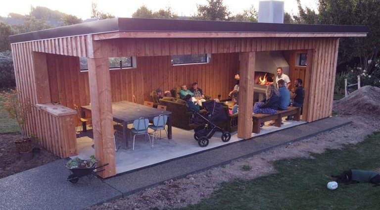 Finished cedar pavilion at dusk with an outdoor fireplace and a table of guests