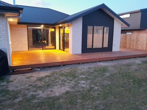 Finished new home at dusk with warm interior lighting and a full-width timber deck