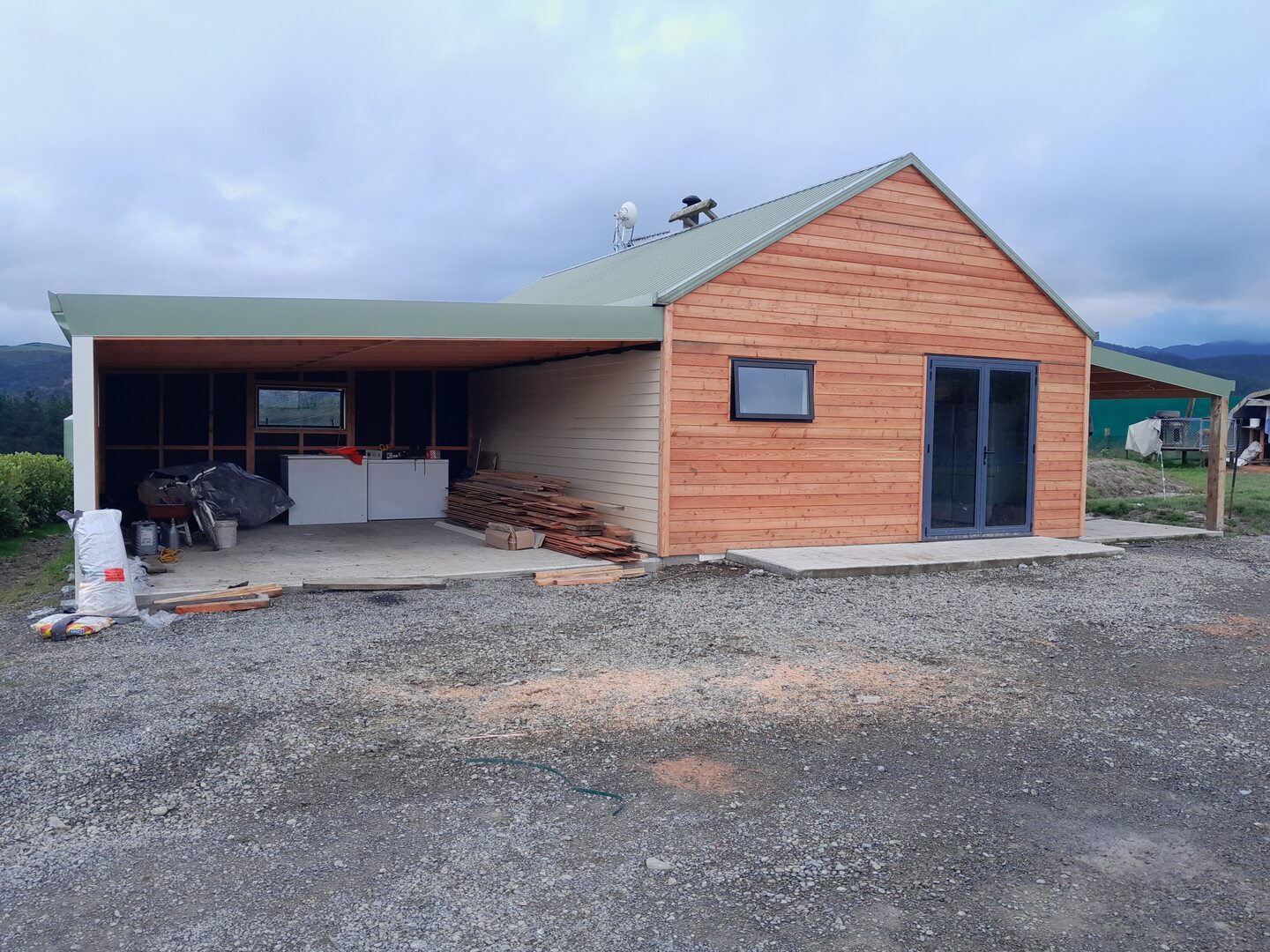 Cedar weatherboard building with a green corrugated steel roof, aluminium double doors and an open lean-to bay alongside for covered storage