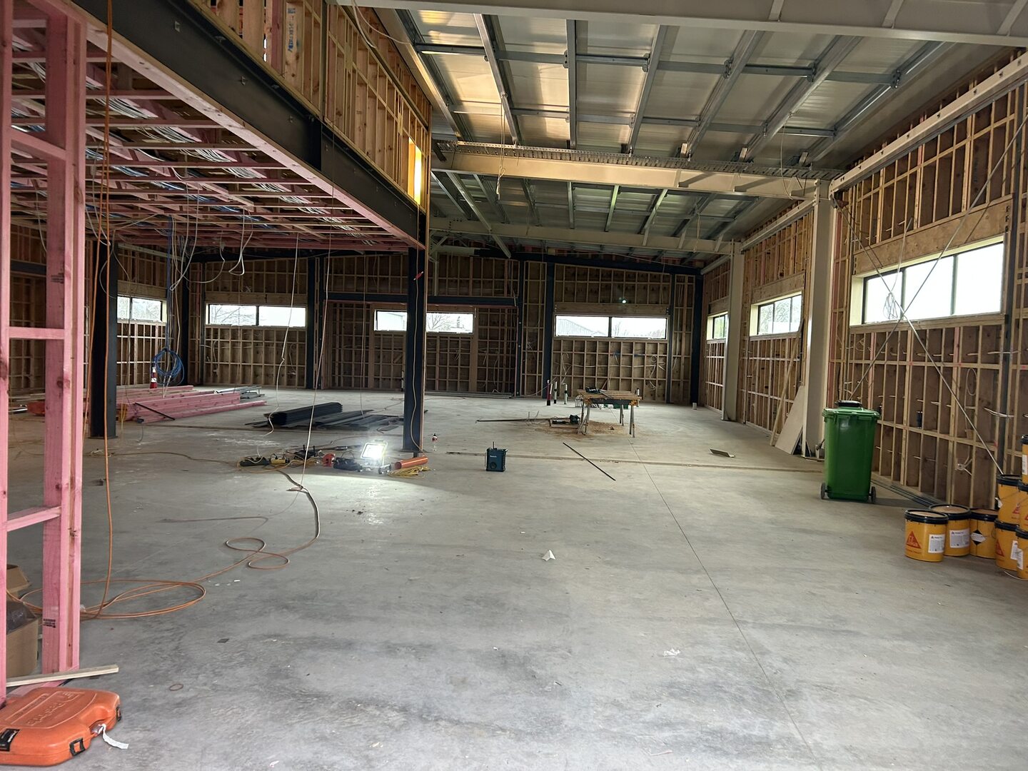Interior of a commercial building at lining stage, with timber wall framing, a steel mezzanine floor over one end, steel roof purlins and a power-floated concrete floor
