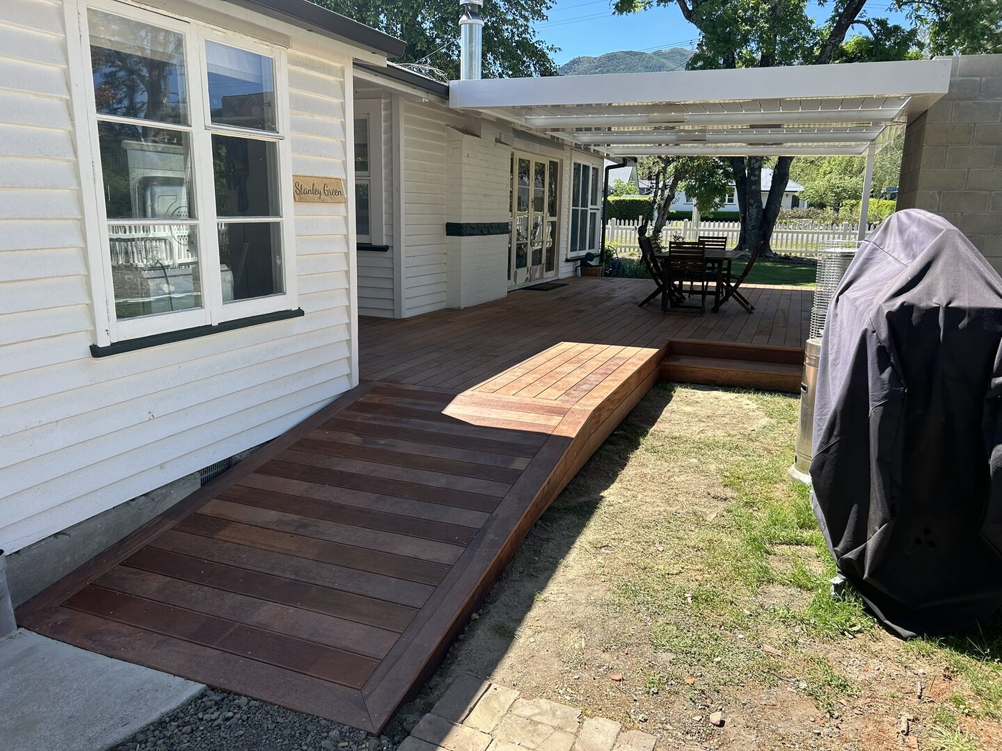 Weatherboard cottage with a dark oiled hardwood walkway running along the wall to a raised deck under a white powder-coated pergola