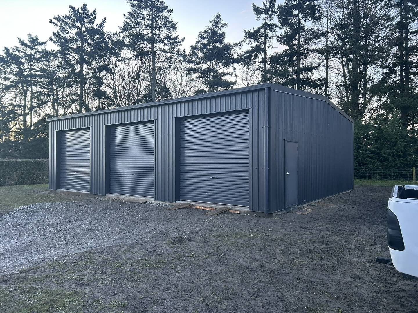 Three-bay garage clad in charcoal profiled steel with three roller doors and a personnel door on the end wall