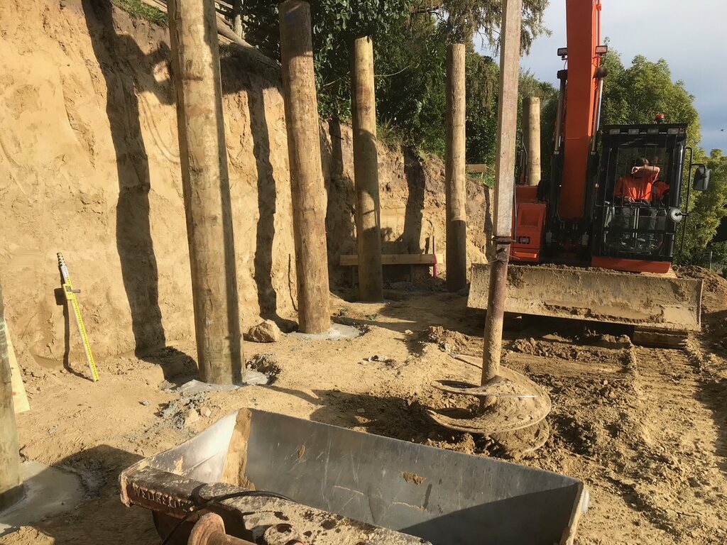 Retaining poles being set into a bank with an excavator alongside