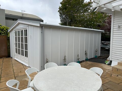 Finished garden room with arched french doors beside a paved outdoor dining area