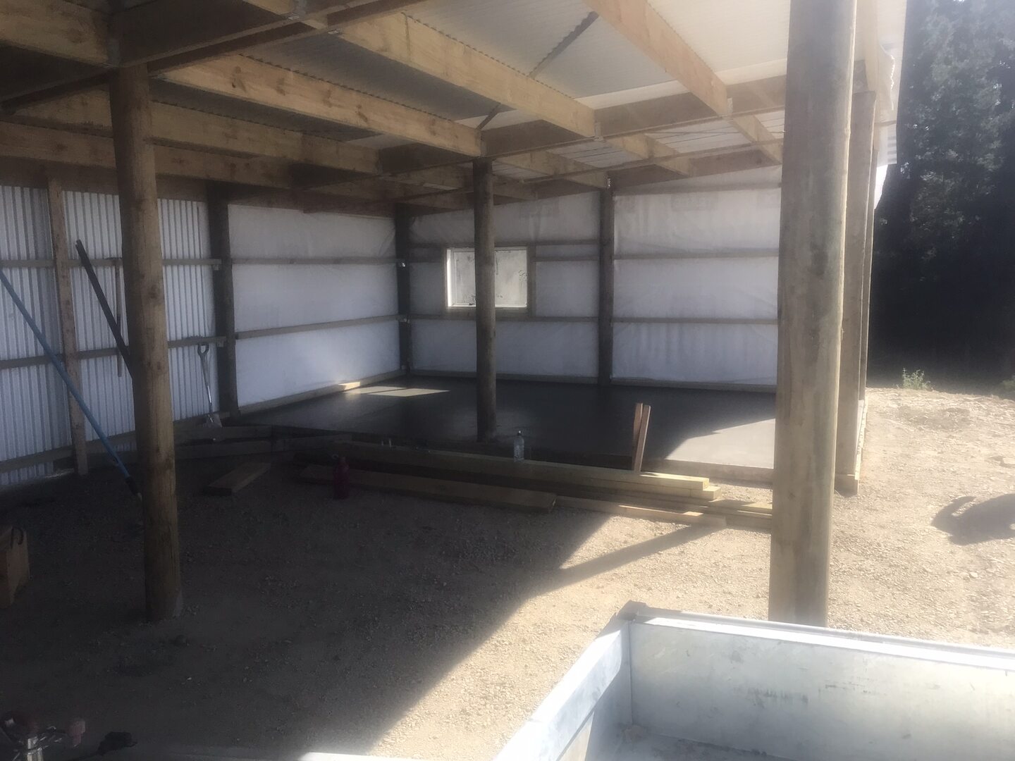 Inside the pole shed, showing round timber poles, timber bearers and rafters, steel diagonal bracing and building wrap behind the profiled steel wall cladding