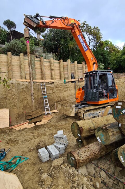 Excavator placing timber rails into a new retaining wall