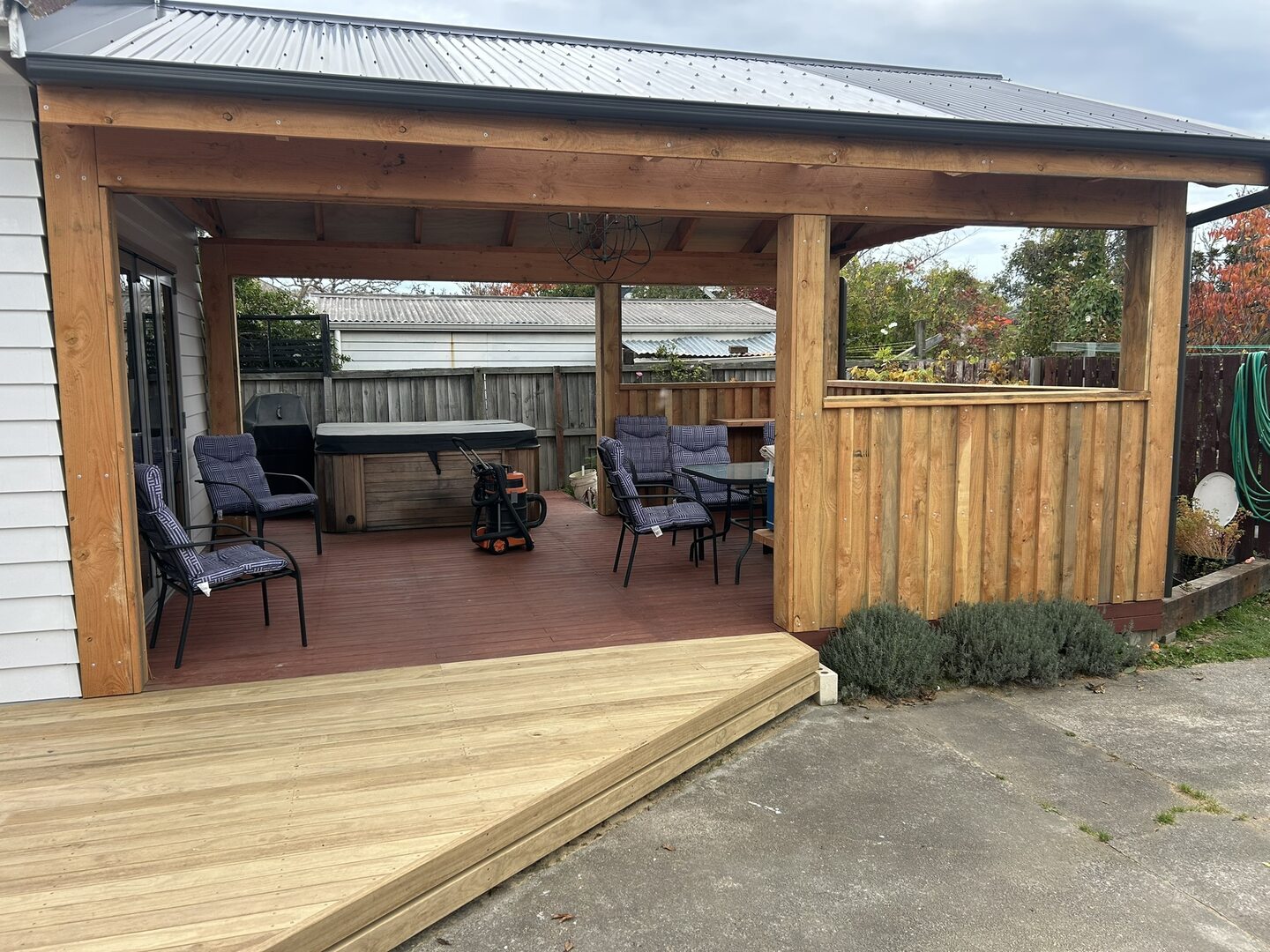 Covered outdoor room with a stained timber deck, cedar balustrade infill and a corrugated steel roof, with a spa pool under cover