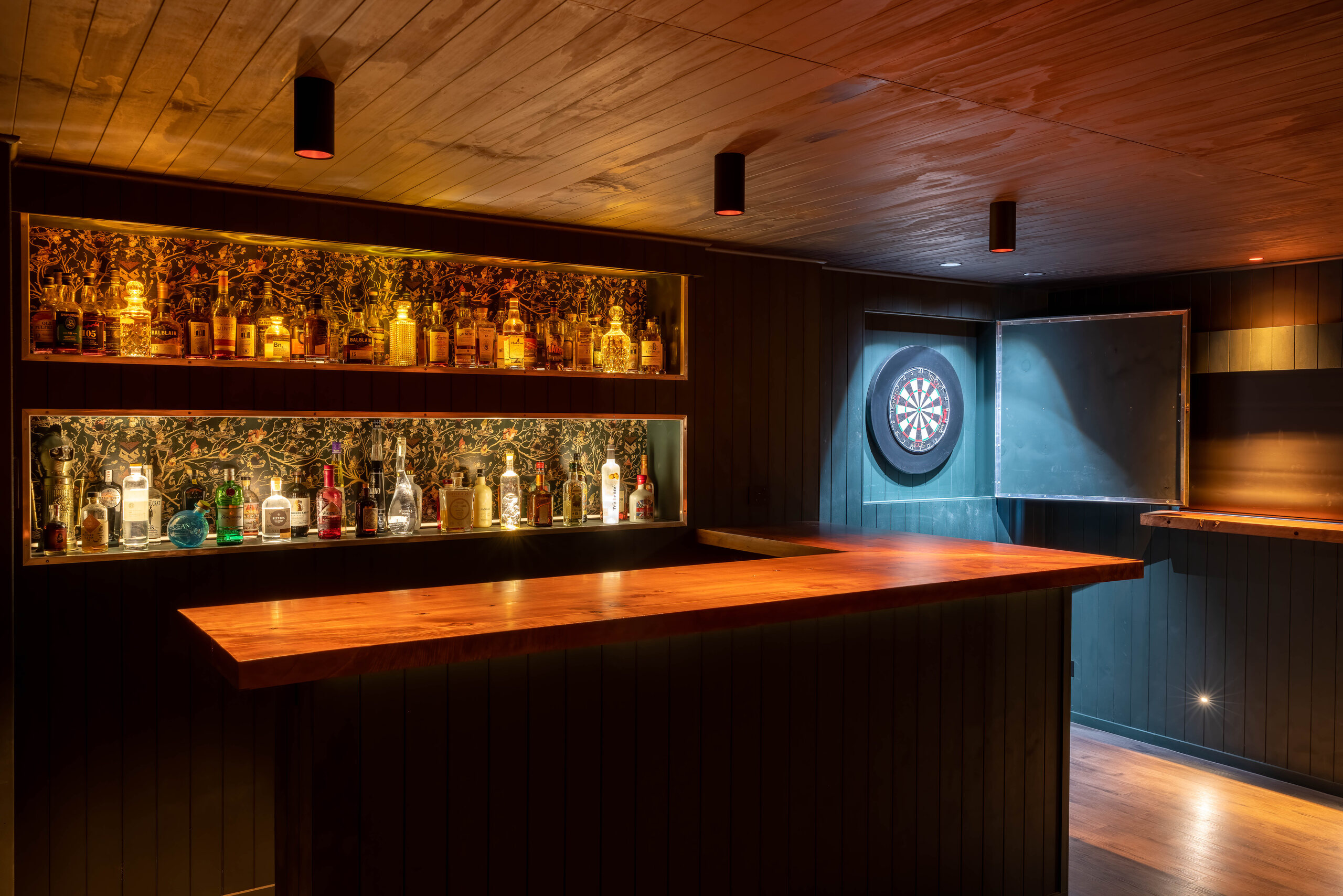 Finished garage bar with timber panelling, pendant lights and a dartboard alcove